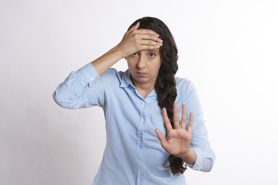 Overwhelmed woman with hand on forehead, making "stop" gesture